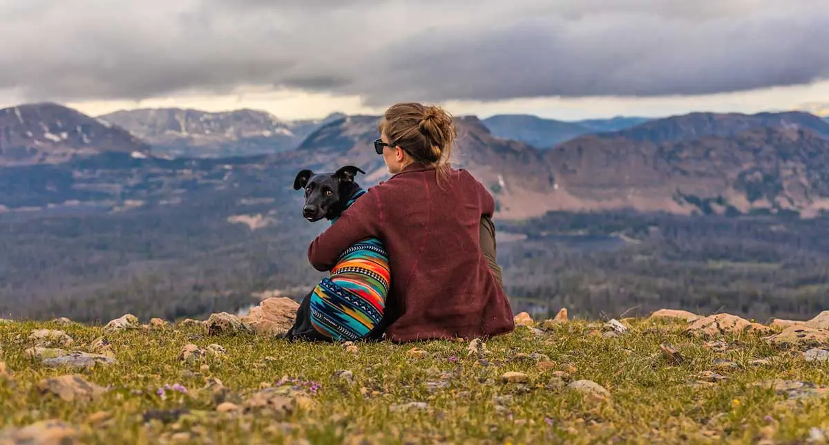 woman sitting with black dog in poncho